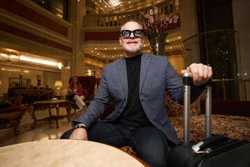 Smiling man in glasses sits in seating area hotel lobby