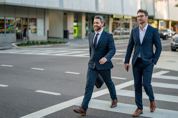 Businessmen couple walking across the crosswalk on american city street outdoor. Cheerful middle eastern businessman walking by street. Portrait of successful business people outdoor.