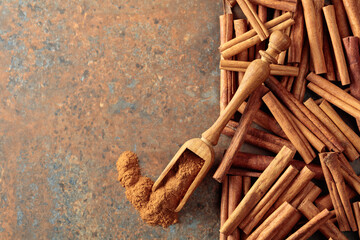 Cinnamon powder in a wooden spoon and cinnamon sticks on a rusty metal background.
