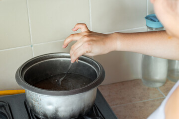girl stirring the water inside the pot to dissolve the added salt.
