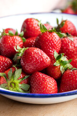 Bowl of fresh strawberries on a wooden board. Fresh ripe delicious strawberries in a white bowl on a wooden background. Close-up.