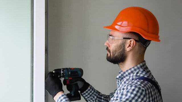 Man in uniform does pvc window installation with a screwdriver in office or apartment.