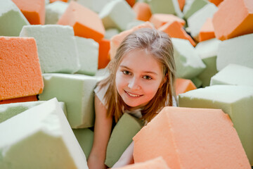 Pretty child girl in trampoline park having fun in colorful soft cubes and smiling. Cute preteen...