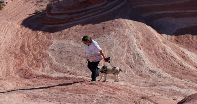 Mature woman hikes with dog at Fire Wave in Valley of Fire State Park in the Mojave Desert of southern Nevada.  The Fire Wave is one of the most popular attractions in the park.