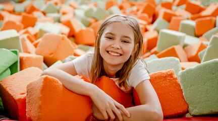 Pretty child girl in trampoline park having fun in colorful soft cubes and smiling. Cute preteen...