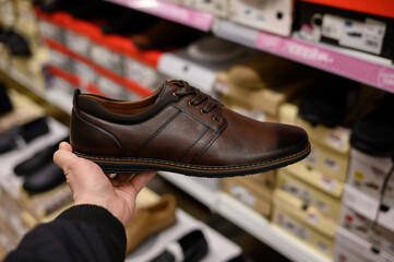 A man chooses shoes in a shopping center in the shoe department, close-up. A man holds brown shoes in his hands.