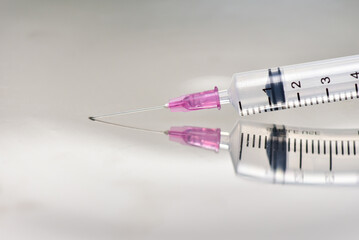 Medical syringe with medicine and a long sharp needle on a white background. Reflection of an object on a surface as in a mirror. Amazing macro.