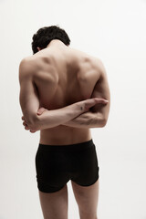 Relief, strong, muscular back. Rear view of young man posing shirtless, in black underwear against white studio background. Healthy spine. Concept of male body aesthetics, style, fashion, men's beauty