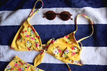 Striped beach towel, floral yellow swimsuit, sunglasses and mesh bag with peaches. Cute beach essentials. Top view.