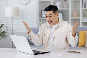 Asian working remotely from home office with laptop, businessman received notification of good achievement results, freelancer satisfied with work rejoices and celebrates victory and triumph.