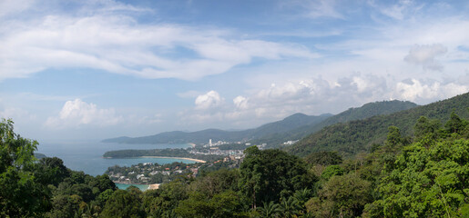 Fototapeta na wymiar Panoramic view from the Karon viewpoint on Phuket Island. In the distance are Patong, Karon, Kata beach. Around are green hills covered with tropical jungle. Sunny, clear day, good weather.