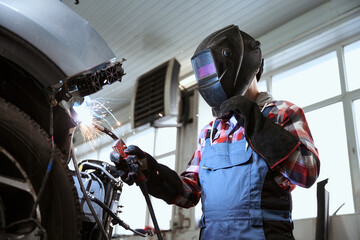 Welder in a welder mask works in car repair shop