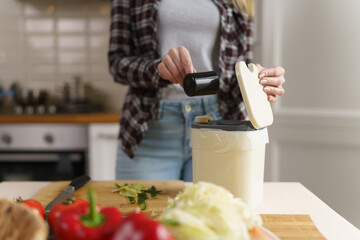 Woman pouring bokashi ferment bran in a compost container for recycling. Female peson using composter bin for organic food waste