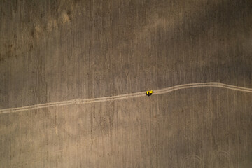 Top drone view of a yellow retro car on a dusty road in a field agriculture