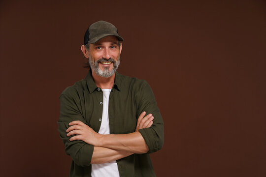 Happy Smiling man. A fisherman in a baseball cap and green shirt stands cross-legged against a brown background with copy space.