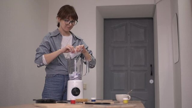 a woman in a blue shirt tears a sheet of paper into pieces and throws them into a blender container. real time video. High quality Full HD video recording