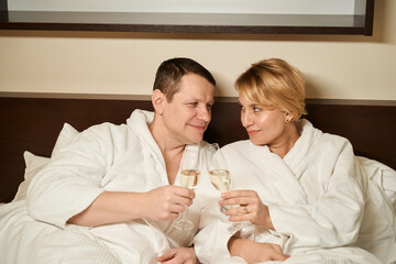 Obraz na płótnie Canvas Middle-aged couple in love enjoying champagne in bed