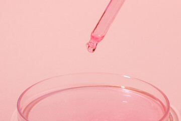 Pipette with dripping pink liquid. Or rose gold. On top of a Petri dish with pink liquid. On a pink background. Laboratory, chemistry, medicine. Cosmetic research. glitter.