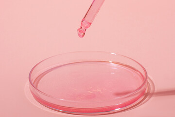 Pipette with dripping pink liquid. Or rose gold. On top of a Petri dish with pink liquid. On a pink background. Laboratory, chemistry, medicine. Cosmetic research. glitter.
