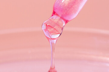 Pipette with dripping pink liquid. Or liquid rose gold. Close-up. On a pink background. Laboratory, chemistry, medicine. Cosmetic research. shine.
