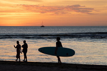 silhouette of person with surfboard and a couple walking the beach during gorgeous sunset