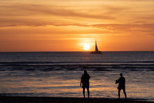 couple on beach watching sunset and sailboat on vacation