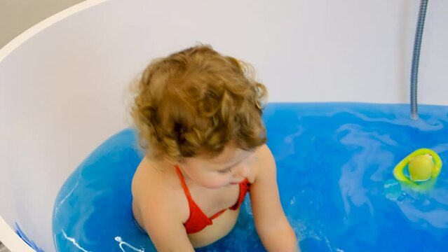 The child bathes in the bath paint blue color. Selective focus.