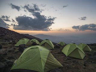 Tent camp of green identical tents on the rocky slope of Mount Ararat at sunset, identical tents a team of tourists on the ascent