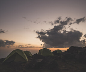 Fototapeta na wymiar Tent camp of green identical tents on the rocky slope of Mount Ararat at sunset, identical tents a team of tourists on the ascent