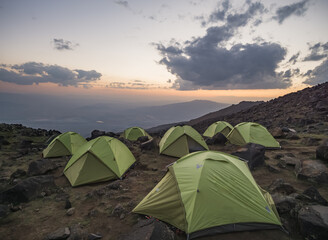 Tent camp of green identical tents on the rocky slope of Mount Ararat at sunset, identical tents a team of tourists on the ascent