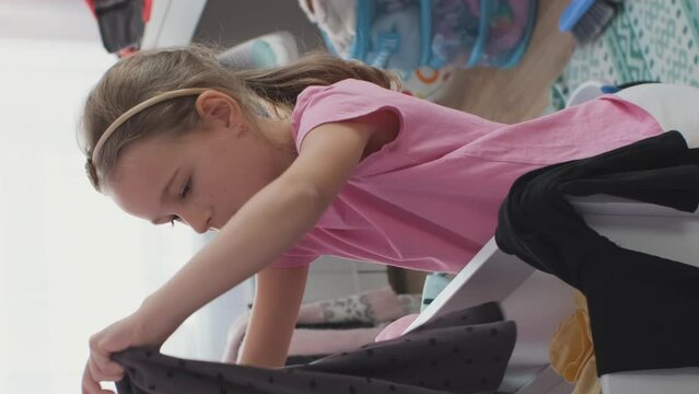 Vertical video. Little girl folding clothes and putting it in the drawers, doing room cleaning at home