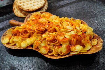 Fried spicy round slices of new potatoes in wooden traditional plate on black oily hob and crunchy...