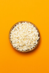 Popcorn inside a wooden bowl on an orange surface.