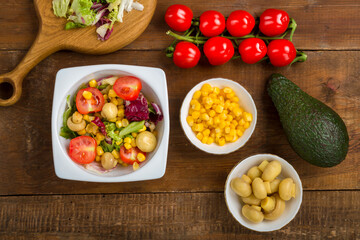 salad with lettuce and cherry tomato with avocado olive oil in a white plate on a wooden table next to all the ingredients.