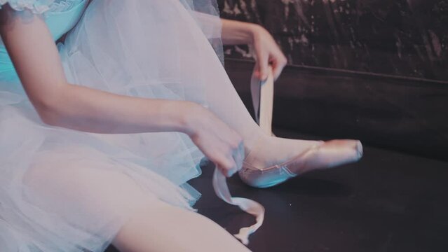 Close up shot of a ballerina putting on her pointe shoes. Graceful ballet dancer tying shoes up before  performance. 4k footage
