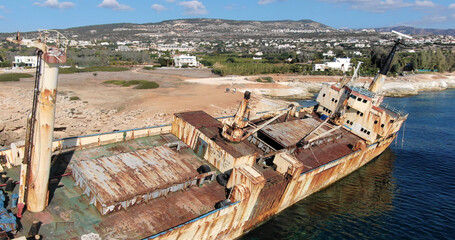 Flying drone over the coastline of the island overlooking an old rusty sunken ship or liner EDRO III, rocky shoreline with vegetation and rocks and clear sea with light foamy waves in Cyprus. 01.03.20
