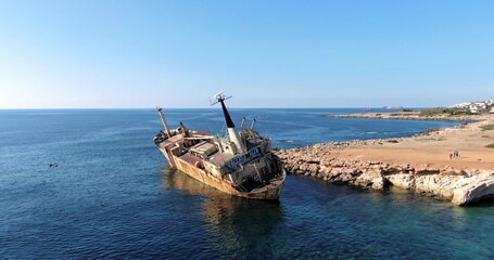 Flying drone over the coastline of the island overlooking an old rusty sunken ship or liner EDRO III, rocky shoreline with vegetation and rocks and clear sea with light foamy waves in Cyprus. 01.03.20