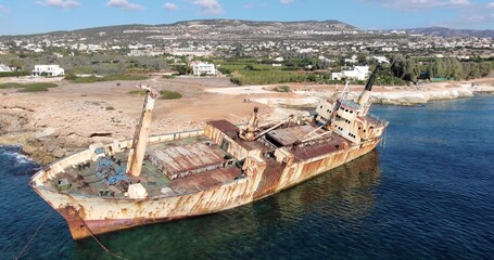 Flying drone over the coastline of the island overlooking an old rusty sunken ship or liner EDRO III, rocky shoreline with vegetation and rocks and clear sea with light foamy waves in Cyprus. 01.03.20