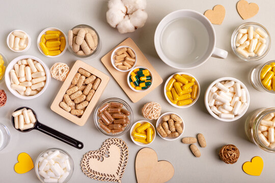 Different Vitamins, Minerals And Food Supplements In Jars And A Cup Of Water From Above On Light Background. Nutrition Supplements In Form Of Pills, Tablets And Capsules To Improve Immune System.