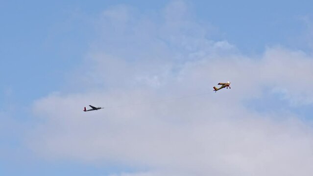 bright yellow plane pulls glider on cable, accelerating it to required speed so that glider can fly itself. Cloudy weather for flying for fun on airplane.