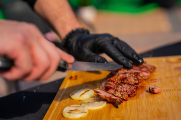 Chef with black rubber cooking gloves slicing steak on wooden board