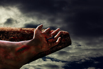 Crucifixion of Jesus focusing on bloodied and bruised hand nailed to wooden cross with dramatic sky background. Easter and Good Friday Christian message.