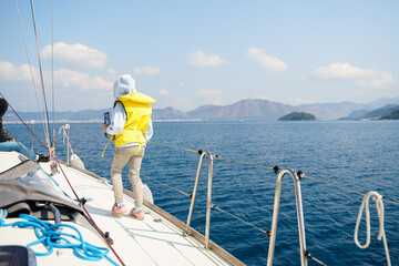 Fototapeta premium Voyage sail on sport sea luxury yacht. Yachting family summer vacation cruise. Children, sailor kid girl sailing in little safe life jacket. Ocean ship boa travel. Enjoy trip on sailboat front deck