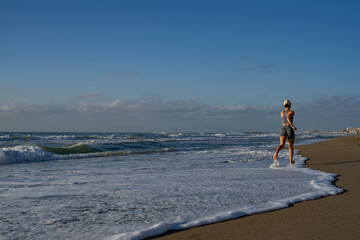 beautiful young girl is engaged in jogging on the seashore rear view