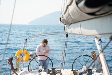 Businessman, owner with mobile phone at steering wheel in voyage sail on sport sea luxury yacht. Yachting summer vacation cruise. Sailing on ocean ship boat travel. Enjoy trip on sailboat front deck