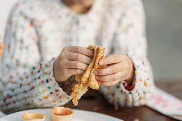 Child's hands holding pancake crepe over plate with toppings