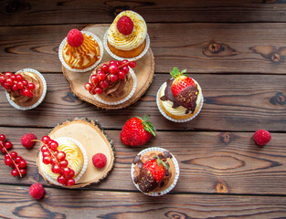 Flat lay chocolate and vanilla cupcakes decorated with fresh berries on rustic wooden background