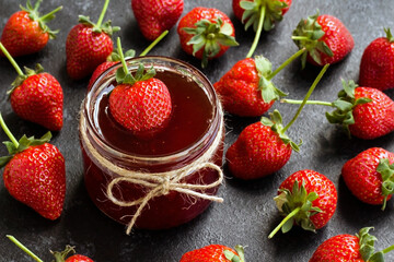 Natural strawberry jam with ripe strawberries on black surface