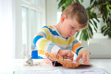  Little boy performing or studying science with wires, connections. Electronic experiment. The child is experimenting at home.