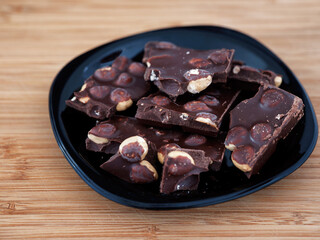 Pieces of broken dark chocolate with hazelnut in a black plate